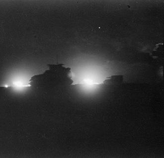 Vehicles silhouetted against the flash of artillery